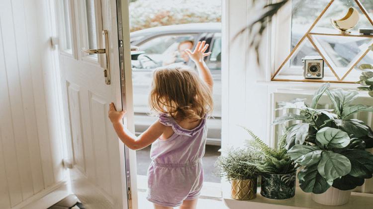 Little girl waving goodbye to her grandparents in a sunny entryway.
